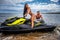 Attractive couple of a girl and shirtless muscular male have fun with a jet ski on a seacoast.