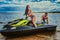 Attractive couple of a girl and shirtless muscular male have fun with a jet ski on a seacoast.