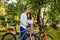 Attractive couple of young adults is in the city park with their bikes, man embracing a woman. Couple of cyclists is outside