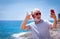 Attractive crazy senior man taking selfie at the sea, wearing red headphones and sunglasses. Carefree retired having fun using