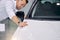 Attractive customer man stands next to white luxurious car in dealership