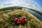 The attractive cyclist sitting on the grass on the meadow with mountain bike above river.