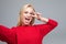 Attractive dark-eyed blonde female take selfie dressed in red sweater against gray background, stretching arm to camera