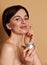 Attractive delighted Caucasian woman holding a jar with anti-aging moisturizing smoothing cream and applying it on her face,
