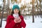 Attractive delightful stunning young woman in red coat and green knit woolen hat with a thermo mug in her hands enjoying a coffee