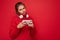 Attractive dissatisfied young brunet woman wearing red sweater isolated over red background wall holding and using