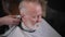 attractive elderly man with beard sitting in barbers chair doing modern haircut with trimmer in popular barbershop