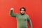 Attractive emotional hispanic man is standing in front of the red wall, pointing his finger down, frowning, feeling amazed when