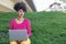 Attractive entrepreneur woman with afro hair and smiling, works sitting and concentrated with her laptop in a quiet park with
