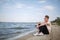 An attractive fellow in a white T-shirt sitting on a riverbank on a natural blurred background.