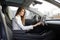 Attractive female driver in formal wear, operating the touchscreen on the dashboard in her electric car inputting data