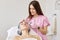 Attractive female laying with closed eyes on cosmetic chair in beauty parlor, having medical cap on head and white towel. Charming