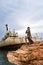 Attractive female model posing on a rocky cliff of the Mediterranean coast with a freighter shipwreck in background