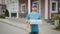 An attractive food delivery man stands on the street with an order. A man in a blue T-shirt and a cap is working.