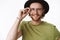Attractive friendly-looking charismatic young bearded guy in glasses and hat touching frames of eyewear and smiling