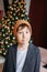 Attractive funny tween boy with dark hair in hat looking at camera on christmas tree background