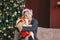 Attractive funny tween boy with dark hair in santa hat hugs gift box on christmas tree background