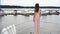 An attractive girl in a dress stands on a boat on the background of other boats on the pier and turns