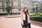 Attractive girl with long curly hair posing on steer on building background. She wears black long dress, pink jack