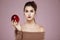 Attractive girl looking at camera holding red apple over pink background. Copy space.