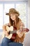 Attractive girl playing guitar in western hat