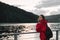 Attractive girl in a red raincoat stands by the lake and poses for looking into the camera. Hiker woman on evening walk and