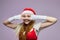 Attractive girl in a Santa hat presses her hands to her face and looks through her fingers
