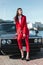 Attractive girl standing next to a retro sport car on the sun. Fashion woman in a red suit and sunglasses waiting near classic car