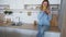 Attractive girl uses smart phone and eats apple, sitting on kitchen surface near sink in kitchen during day.