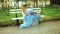 Attractive girl in white and blue dress sits on bench in parkway putting legs in high heeled shoes on bench during photo