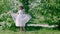 Attractive girl in white summer dress and hat on blooming fruit trees in orchard. Happy girl posing in flowering garden