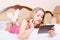 Attractive girl young blond woman in pajamas white socks with tablet pc computer in hands lying on white bed picture