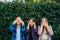 Attractive girls cover their eyes ears and mouth. Three women covering their ears, eyes and mouth on green foliage background