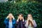 Attractive girls cover their eyes ears and mouth. Three women covering their ears, eyes and mouth on green foliage background