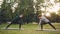 Attractive girls are enjoying outdoor yoga in park practising positions standing on mats. Instructor is speaking