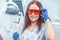 Attractive good-looking portrait of female dentist in clinic sitting on chair near dental unit and wearing red eye glasses for