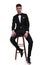 Attractive groom in black tuxedo sitting on a wooden chair