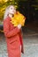 Attractive happy dreamy girl in a red coat smiling joyful and blissful holding autumn leaves outside in her hand in a