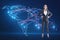 Attractive happy european businesswoman with hands on sides and glowing map and connections on blue background. Global network and