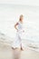 Attractive happy mature tourist blonde woman in long white dress on asian sand tropical beach