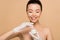 Attractive happy nude asian girl in latex gloves applying face cream