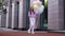 Attractive happy red-haired girl walking on city street with large fountain of colorful balloons.