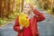 Attractive happy woman in red polto smiling joyful and blissful holding autumn leaves outside in her hand in a colorful