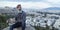 Attractive hipster with a beard is sitting on a rock high over Athens City with Acropolis view