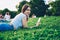 .Attractive hipster girl with braid resting on grass while checking mail on smartphone