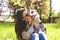 Attractive hipster young woman in sunglasses kissing jack russell terrier puppy in park, green lawn & foliage background. Funny pu