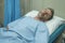 Attractive injured man lying on hospital bed receiving treatment feeling sick and unwell after suffering accident or serious