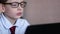 Attractive inquisitive caucasian boy 7-8 years old wearing glasses is studying science sitting at the table holding a gadget in hi