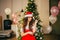 Attractive lady in a Santa Claus New Year`s costume, a red scarlet dress with open shoulders and a hat, playfully looks