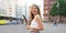 Attractive laughing woman holding smartphone walking on urban background. Looking to the side. Banner cropped view